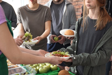 Photo of Volunteers giving food to poor people indoors, closeup