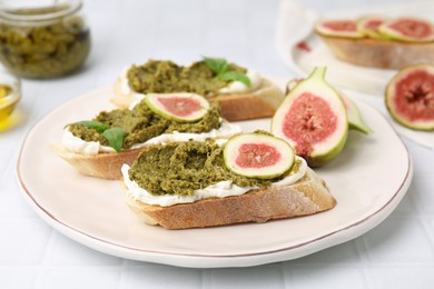 Tasty bruschettas with cream cheese, pesto sauce and figs on white table, closeup