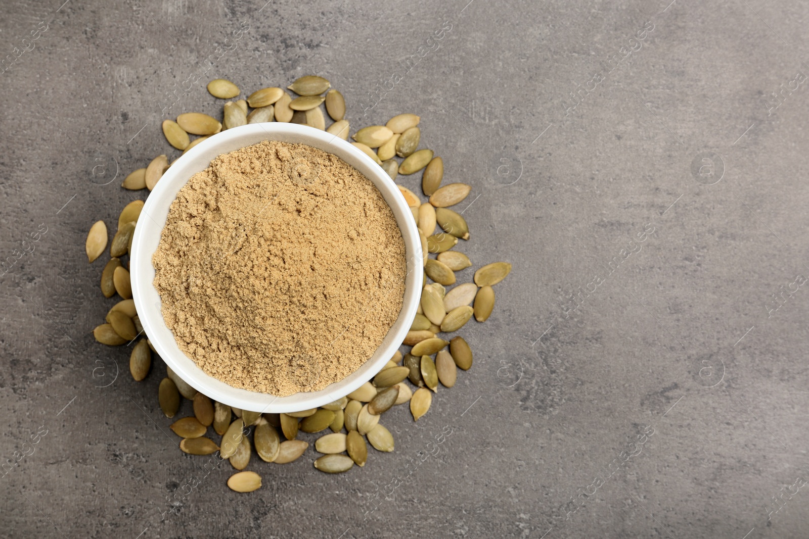 Photo of Bowl with pumpkin flour and seeds on grey background, top view. Space for text