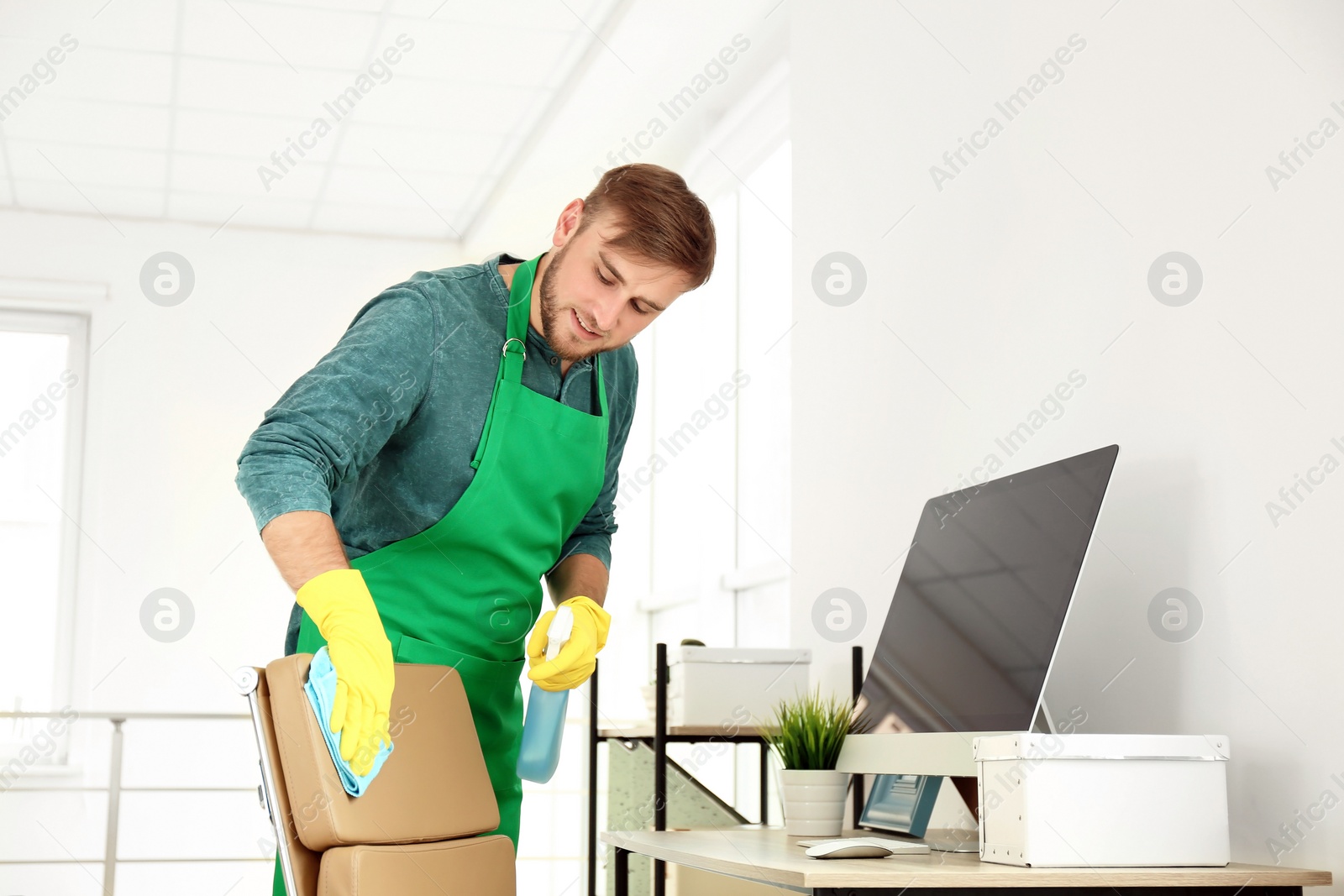 Photo of Young man in apron and gloves cleaning office
