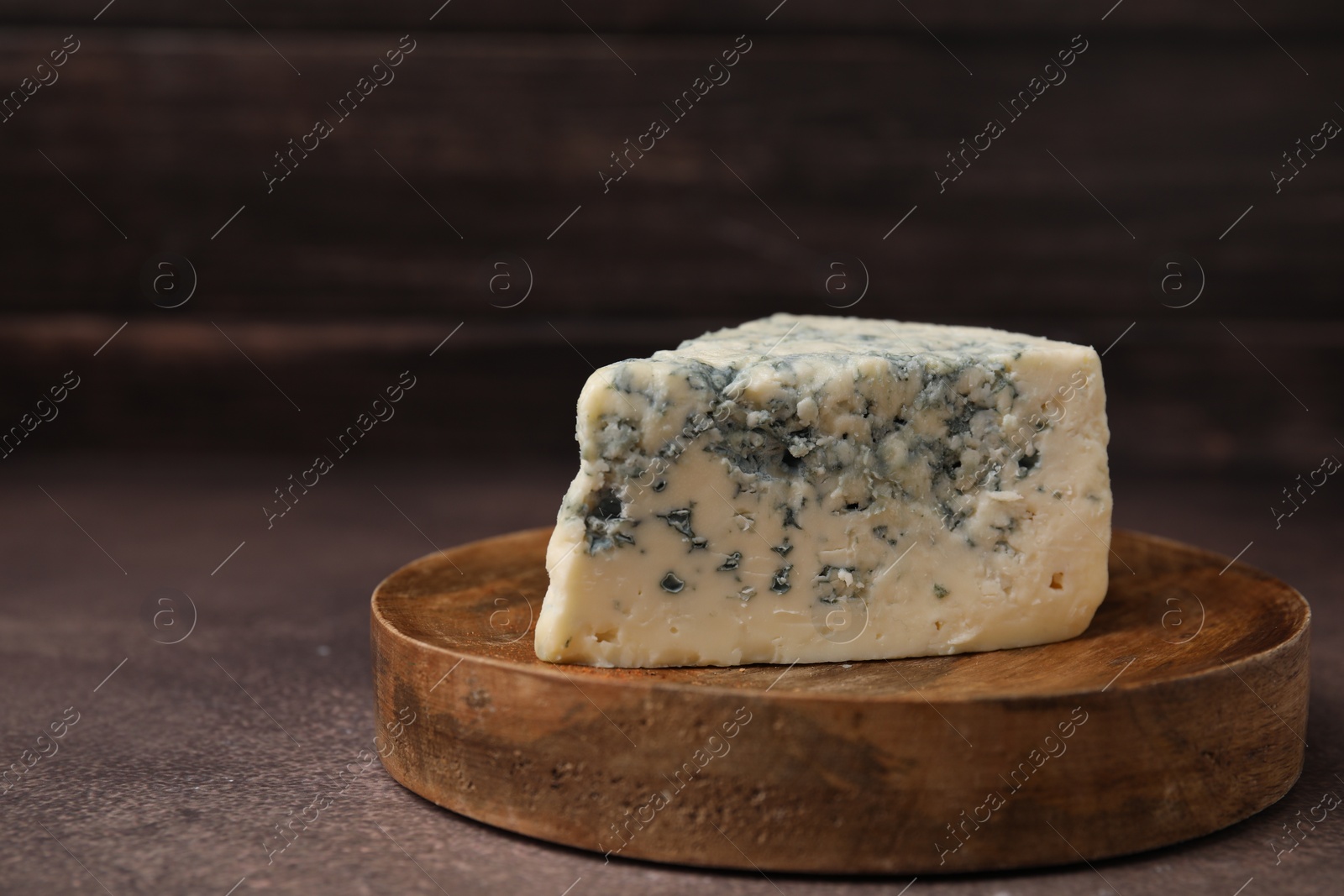 Photo of Piece of tasty blue cheese on brown table. Space for text