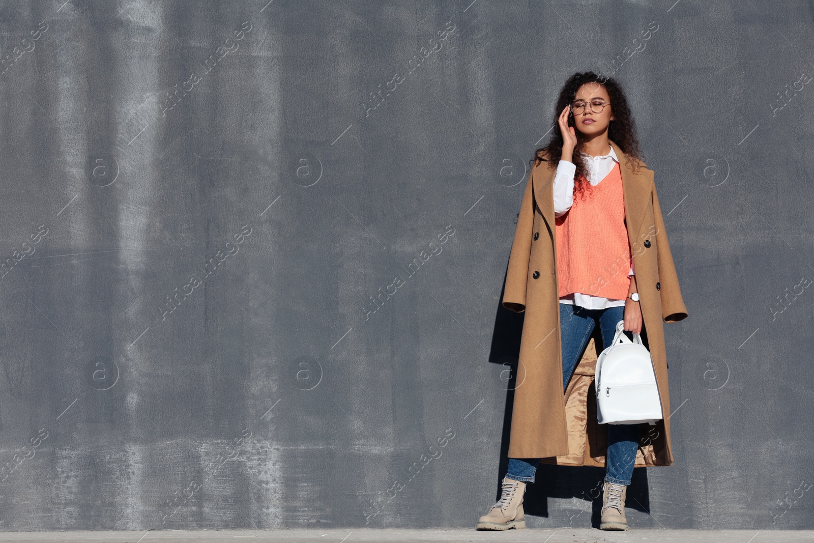 Photo of Full length portrait of beautiful African-American woman with stylish white backpack near grey wall outdoors. Space for text