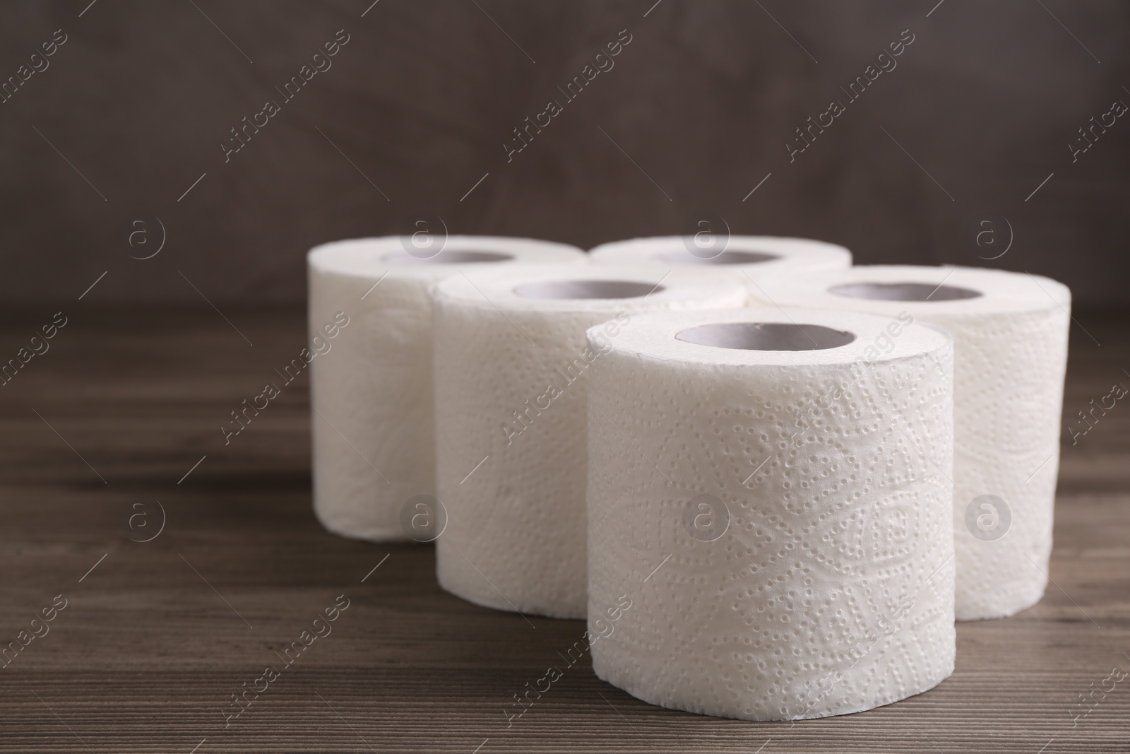 Photo of Soft toilet paper rolls on wooden table, closeup. Space for text