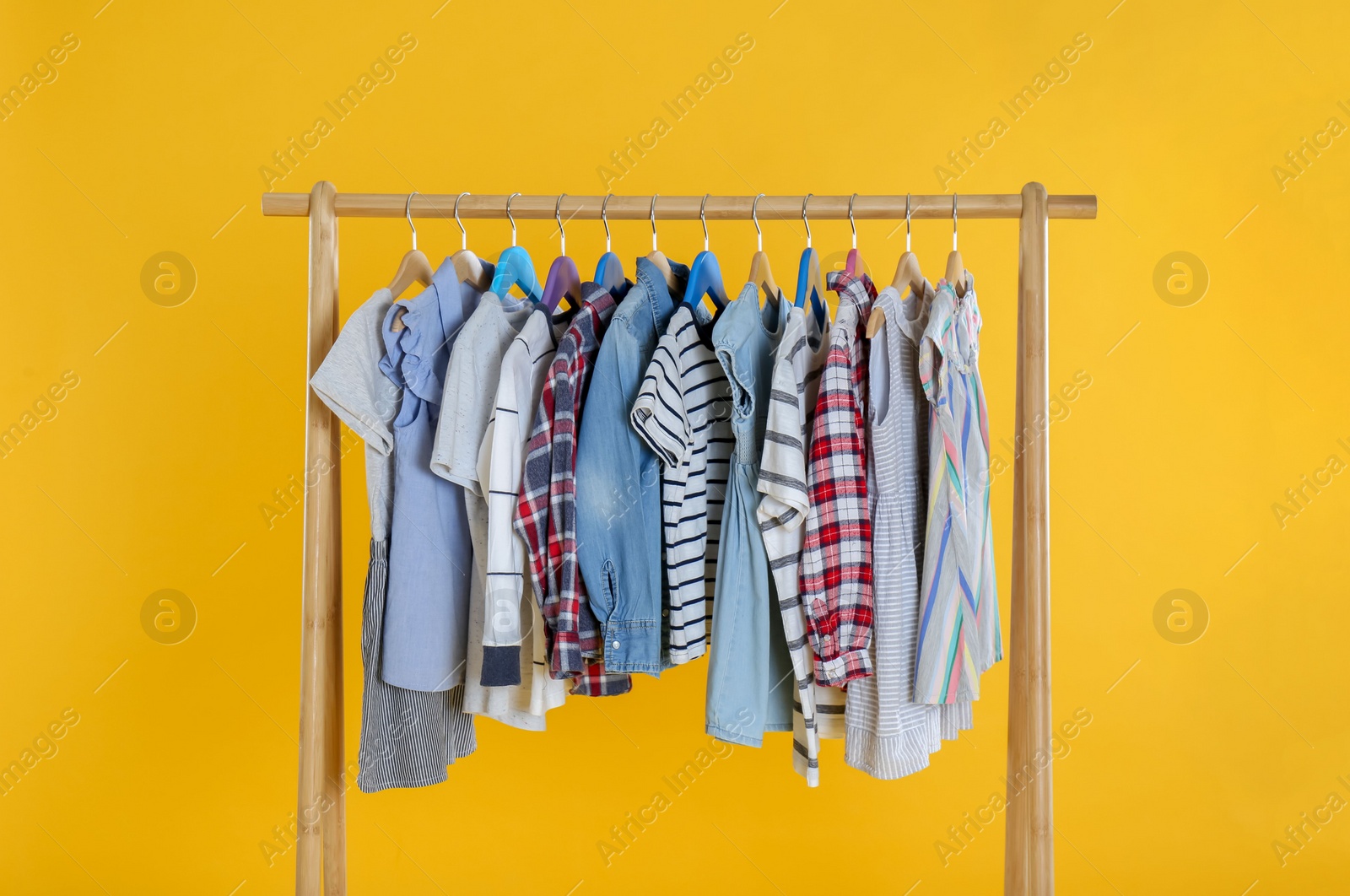 Photo of Rack with stylish children clothes on yellow background