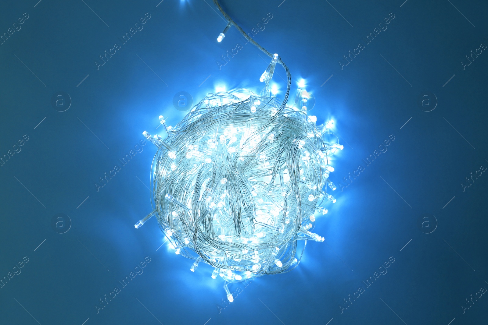 Photo of Glowing Christmas lights on blue background, top view