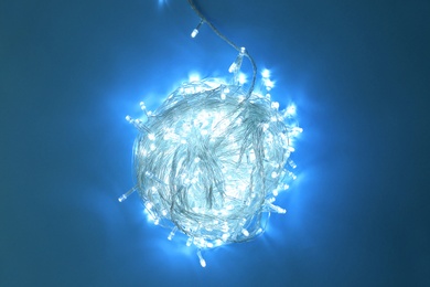 Glowing Christmas lights on blue background, top view