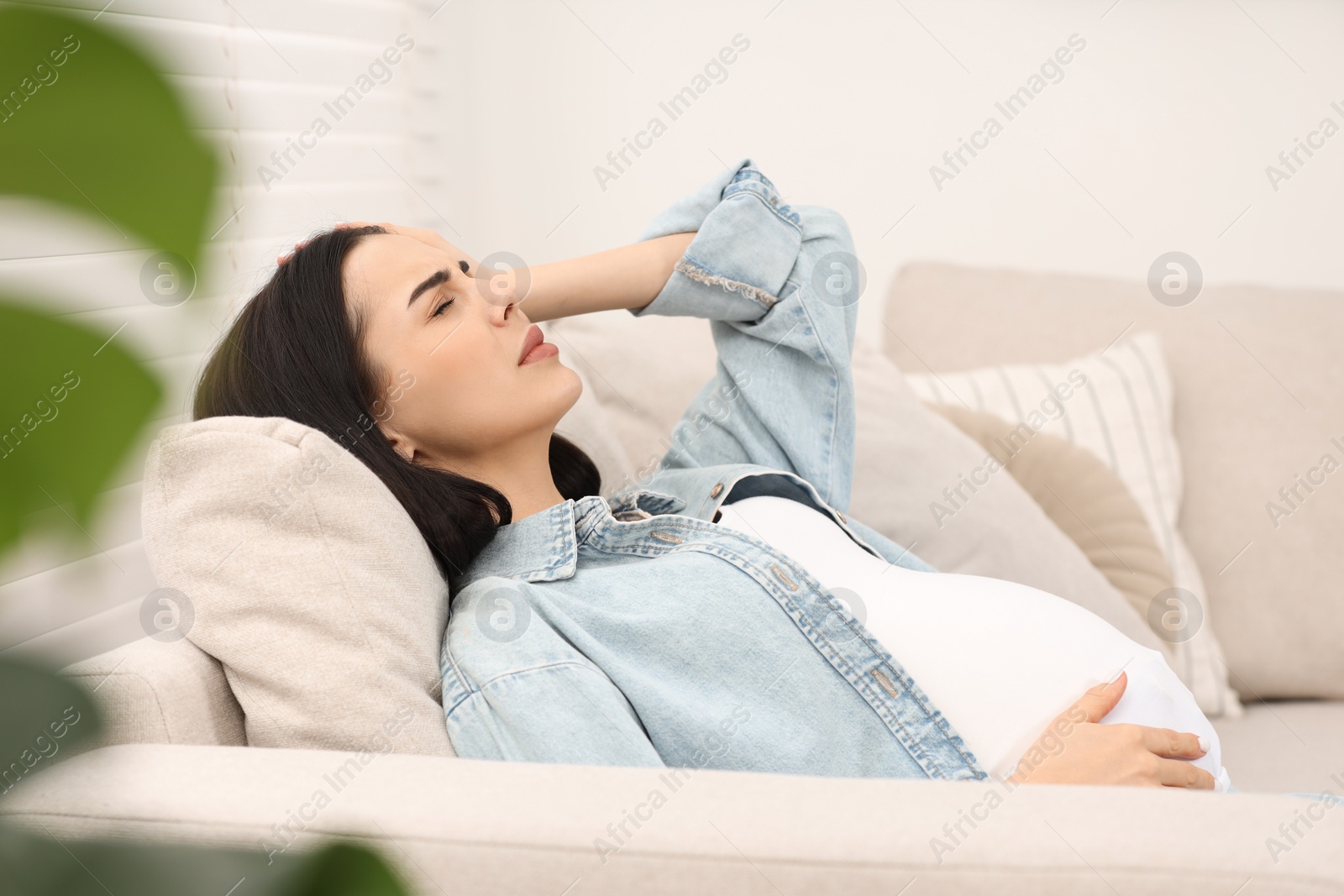 Photo of Pregnant woman suffering from headache on sofa at home