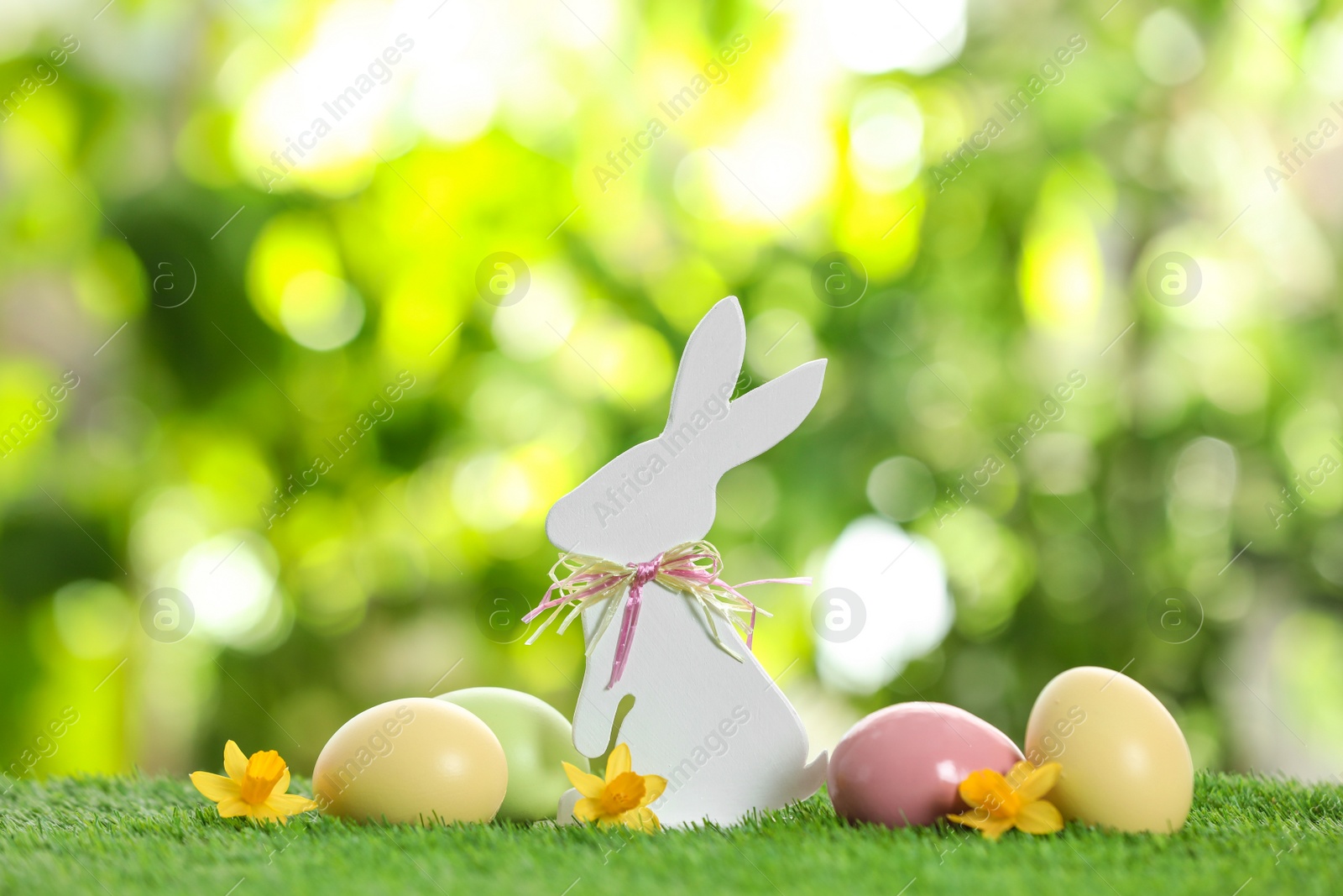 Photo of Cute wooden Easter bunny and dyed eggs on green grass against blurred background