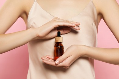 Young woman with bottle of essential oil on pink background, closeup