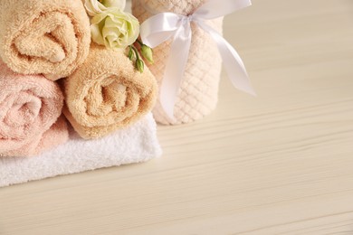 Photo of Soft towels and eustoma flowers on light wooden table, closeup. Space for text