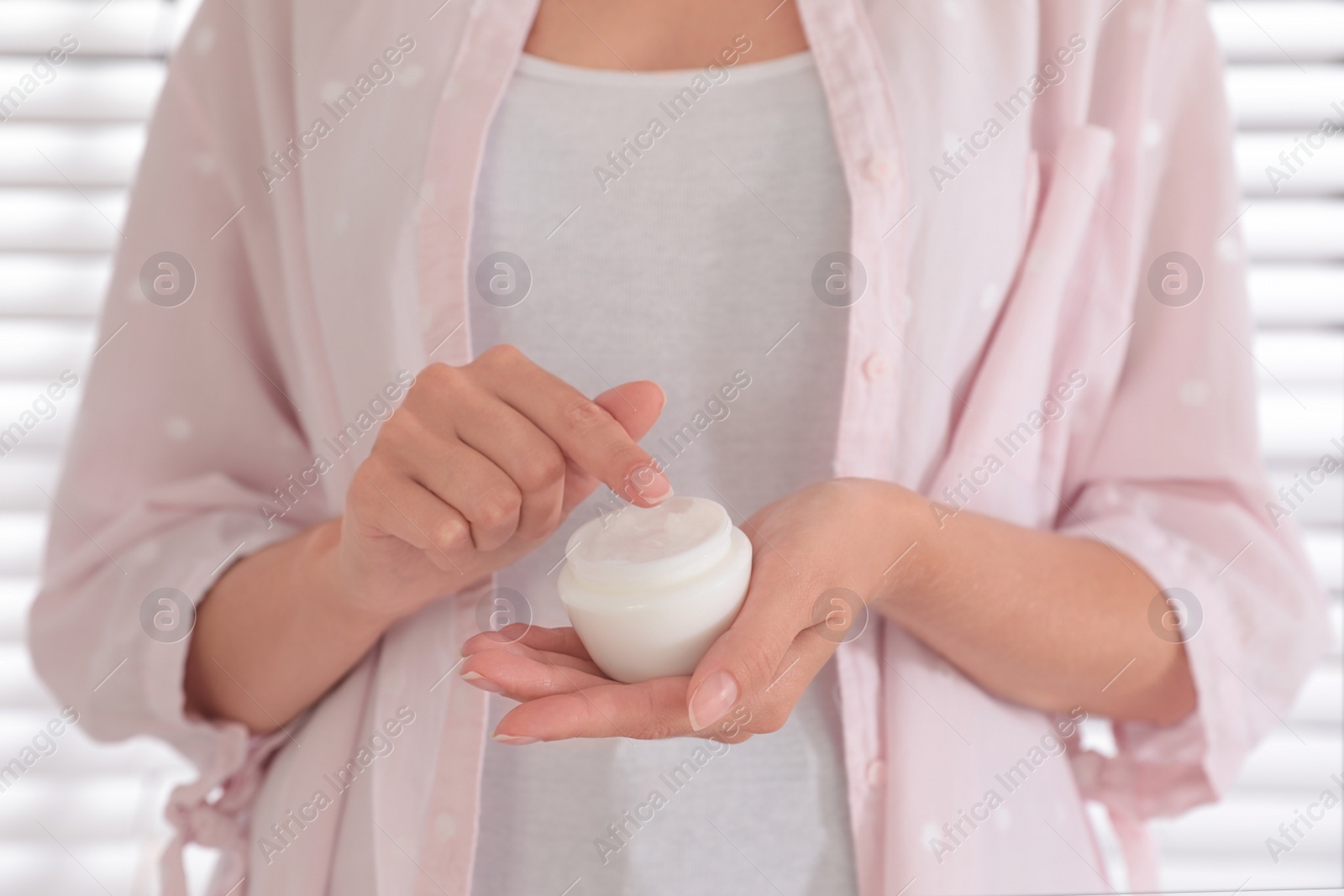 Photo of Woman holding jar with cream near window, closeup