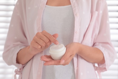 Woman holding jar with cream near window, closeup