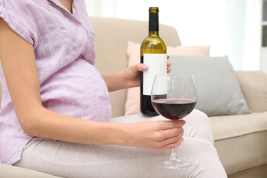 Photo of Future mother with glass and bottle of wine indoors, closeup. Alcohol abuse during pregnancy