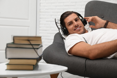 Man with headphones connected to book
on sofa indoors. Audiobook concept