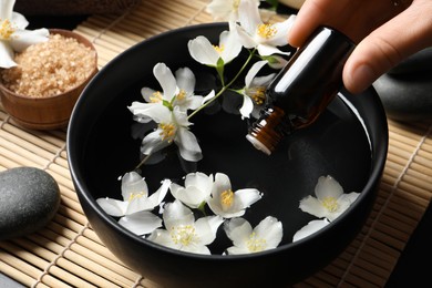 Photo of Woman dripping jasmine essential oil into bowl on table, closeup