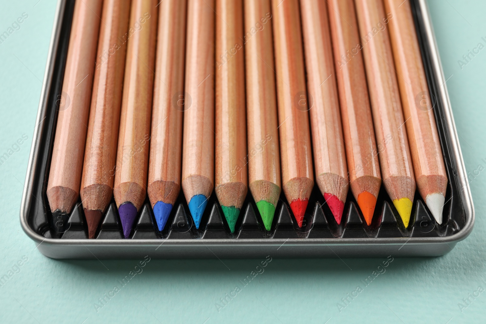 Photo of Box with many colorful pastel pencils on turquoise background, closeup. Drawing supplies