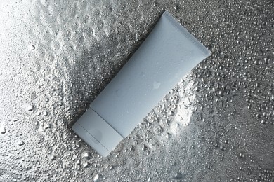 Photo of Moisturizing cream in tube on silver background with water drops, top view