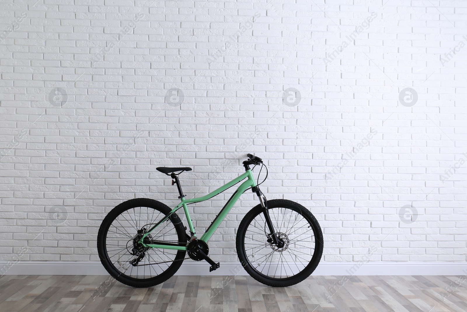 Photo of Modern green bicycle near white brick wall. Space for text