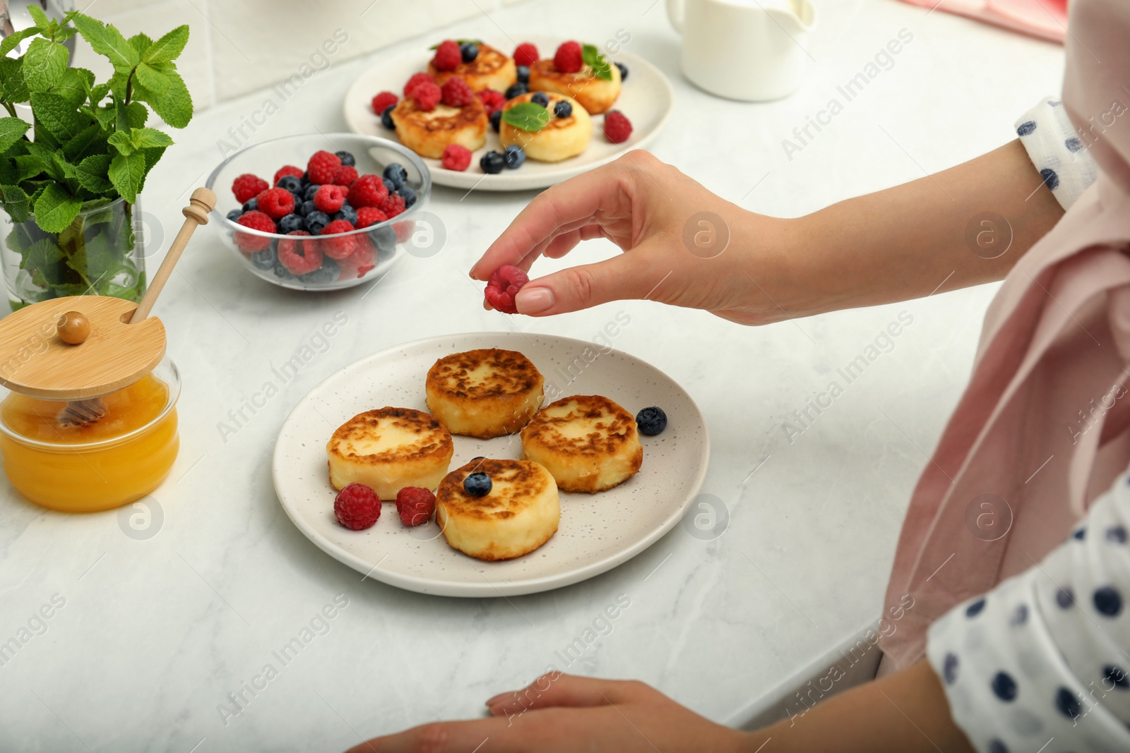 Photo of Woman decorating delicious cottage cheese pancakes with fresh berries at white countertop, closeup