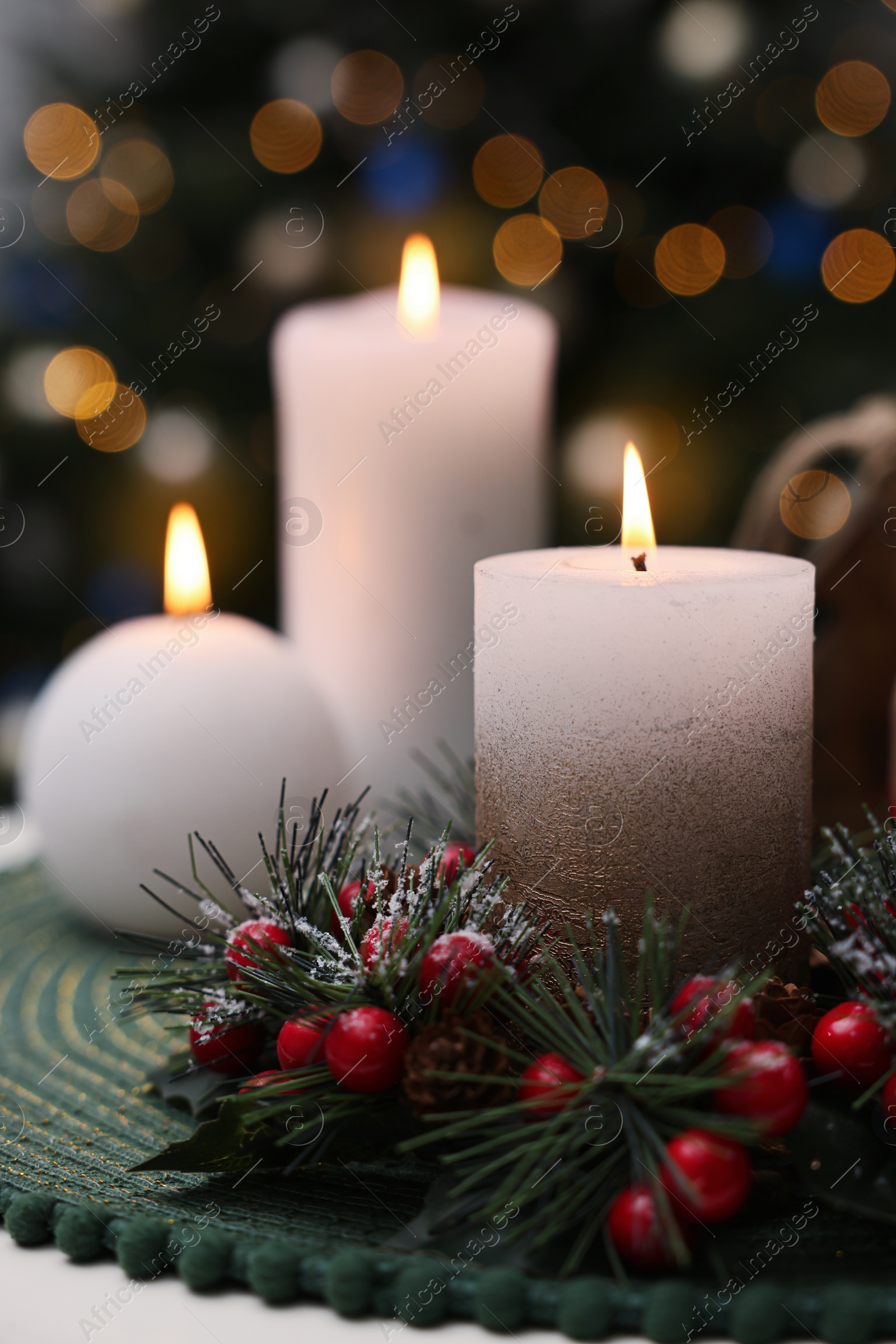 Photo of Beautiful burning candles and Christmas decor on white table against festive lights