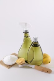 Photo of Bottles of cleaning product, brush, baking soda and lemon on white background