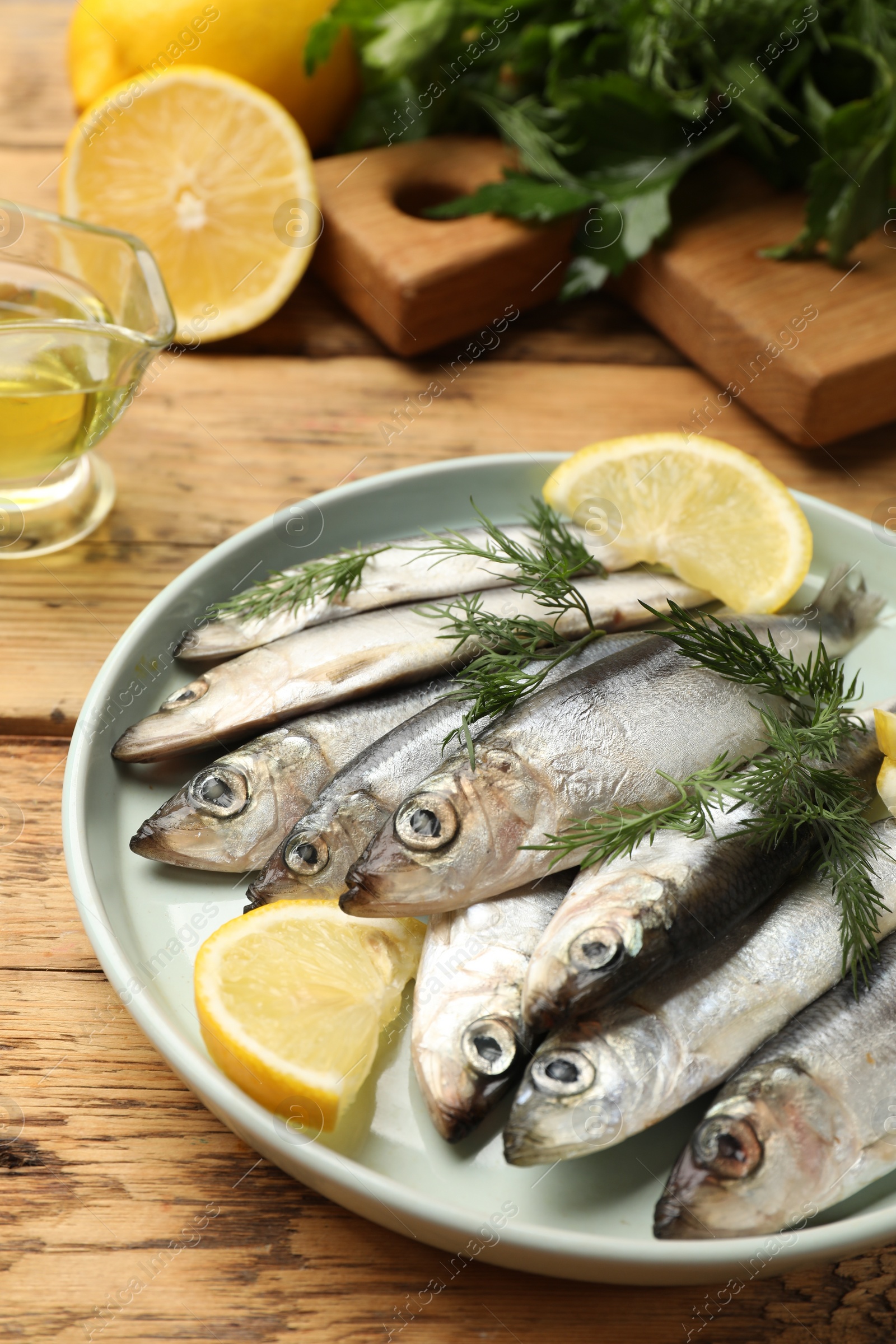 Photo of Fresh raw sprats, lemon and dill on wooden table, closeup