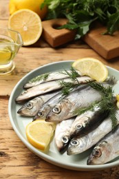 Photo of Fresh raw sprats, lemon and dill on wooden table, closeup