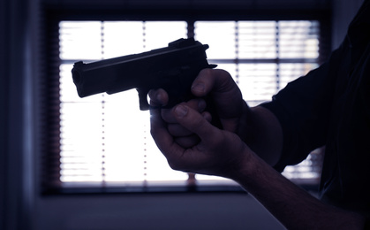 Photo of Man holding gun near window indoors, closeup