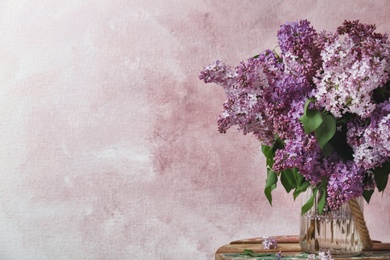 Photo of Vase with blossoming lilac on table against color background. Spring flowers