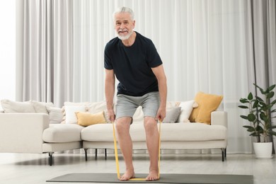 Photo of Senior man doing exercise with fitness elastic band on mat at home