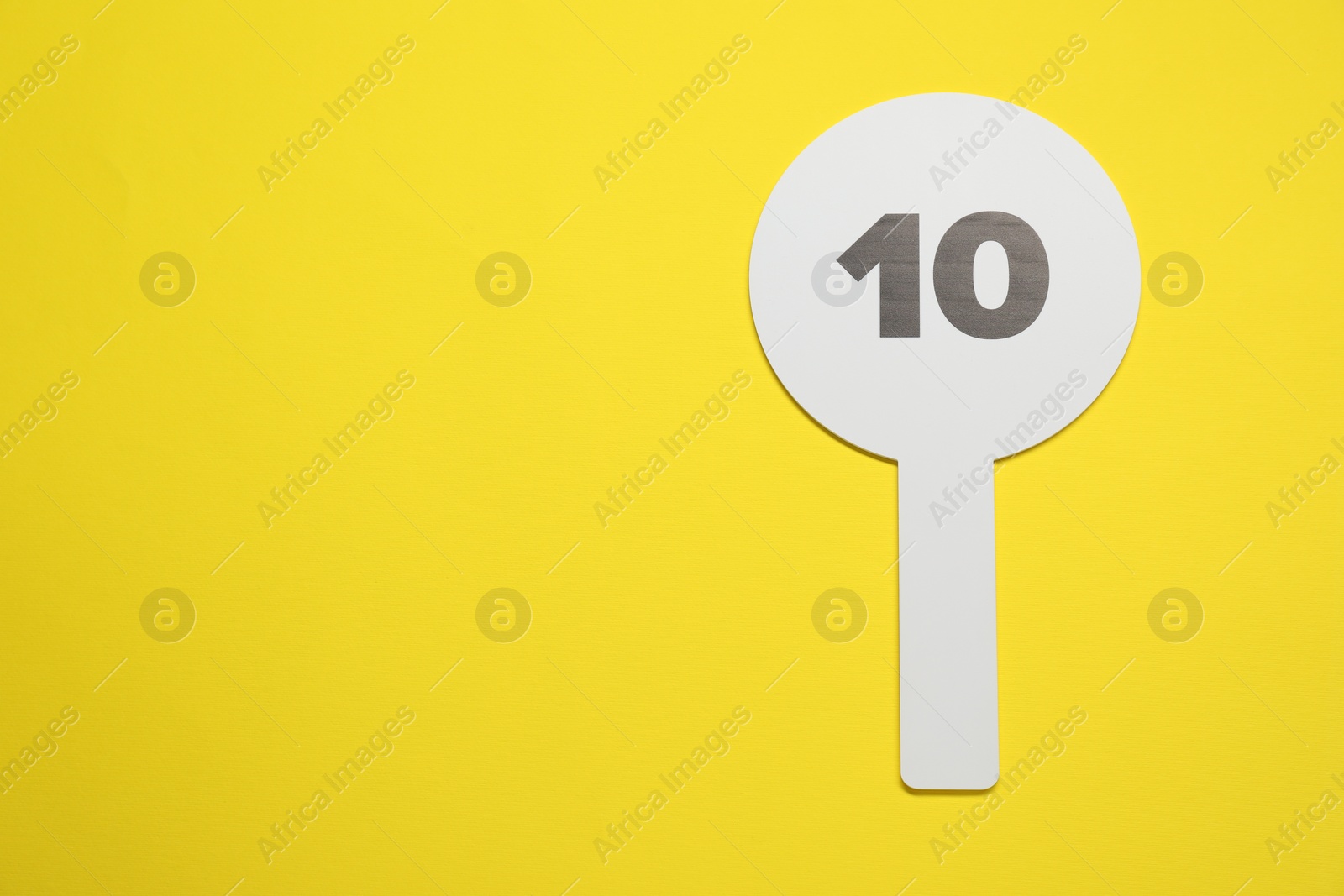 Photo of Auction paddle with number 10 on yellow background, top view. Space for text