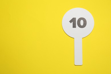 Photo of Auction paddle with number 10 on yellow background, top view. Space for text