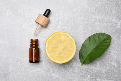 Photo of Bottle of essential oil with lemon slice and leaf on grey table, flat lay