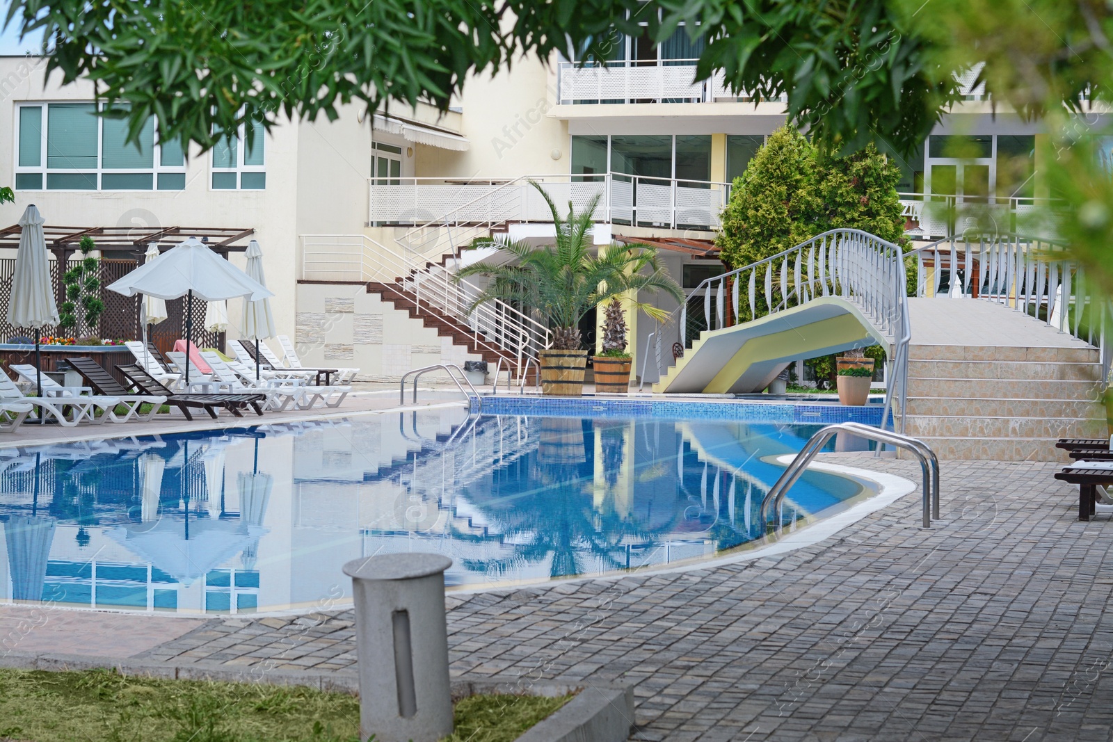 Photo of Outdoor swimming pool with handrails and many empty sunbeds at resort