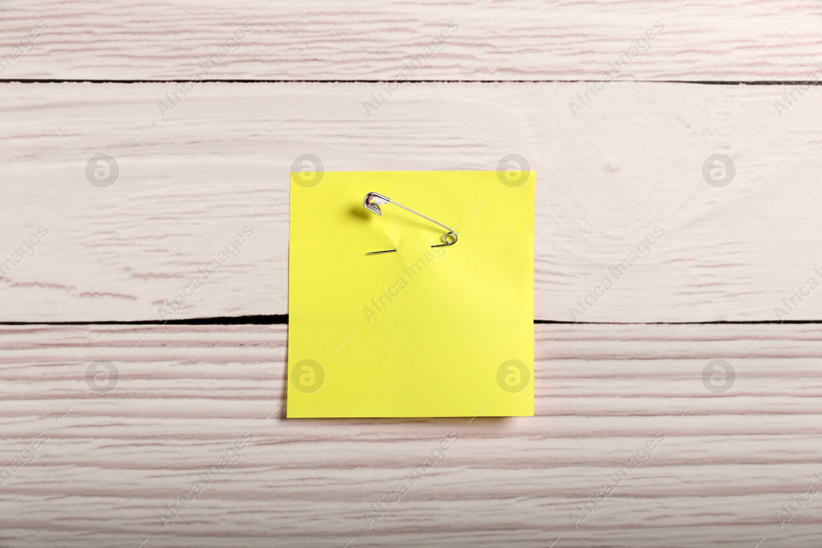 Photo of Yellow paper note attached with safety pin to white wooden background, top view
