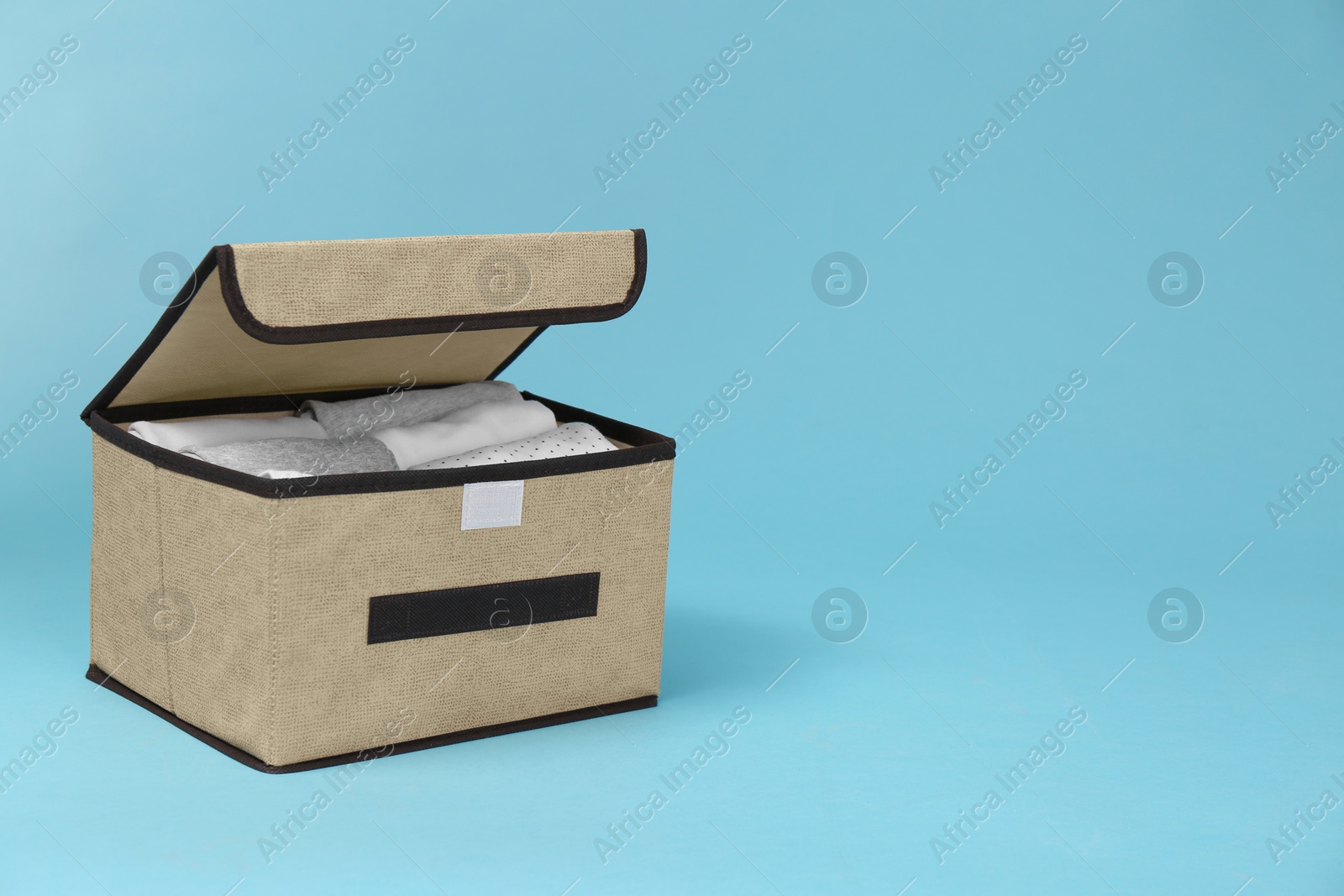 Photo of Textile storage case with folded clothes on light blue background. Space for text