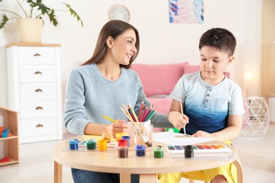 Photo of Cute little child painting at table with his mother in playing room