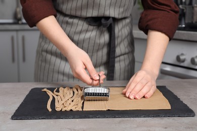 Photo of Woman cutting dough for soba at table in kitchen, closeup