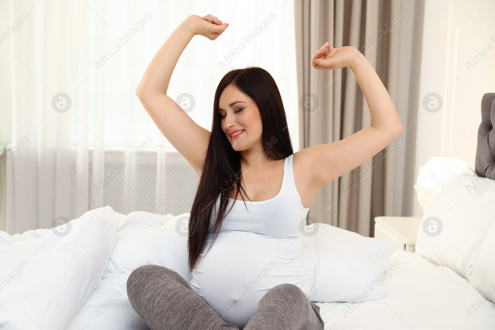 Photo of Beautiful pregnant woman stretching on bed at home