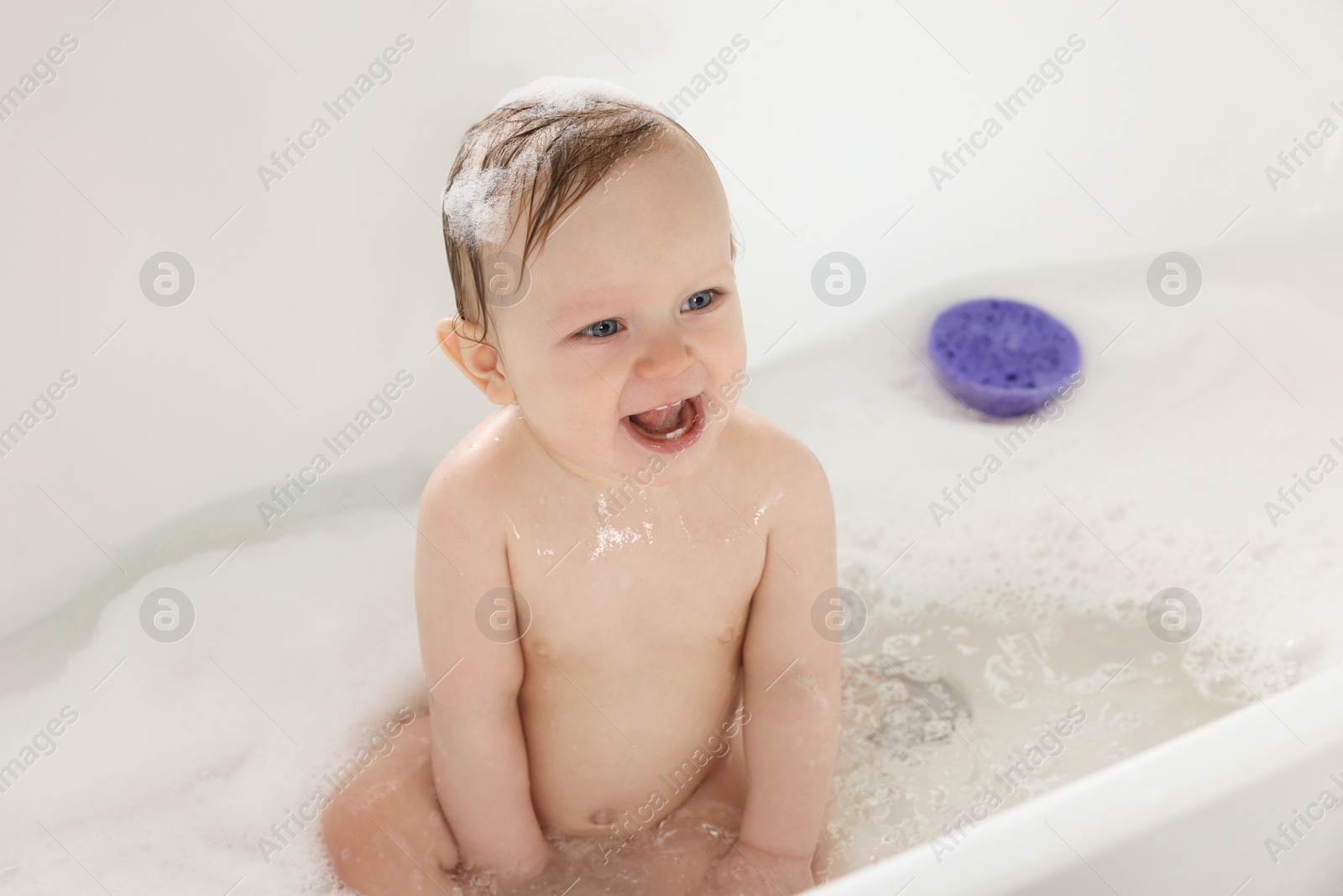 Photo of Cute little baby taking foamy bath at home