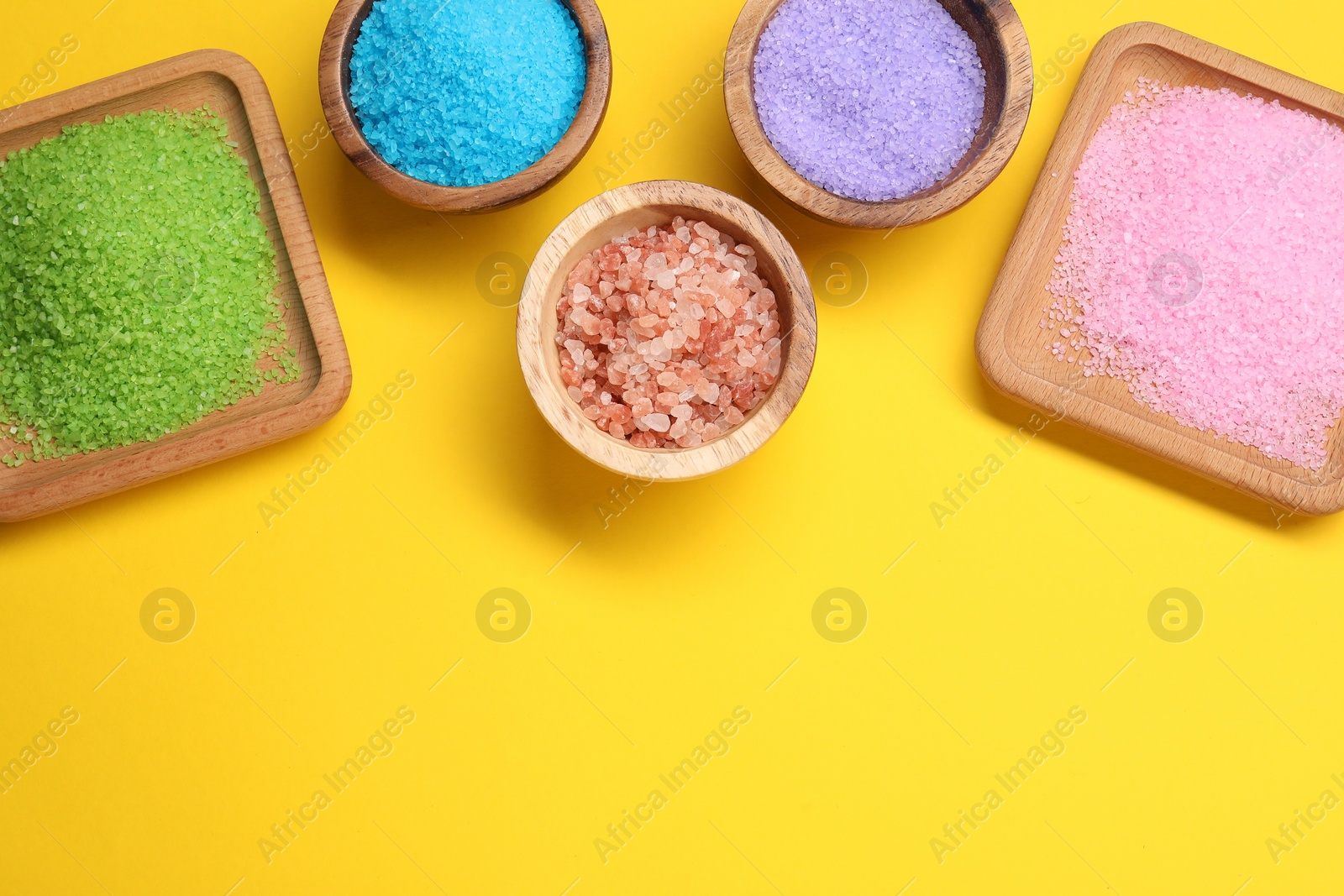 Photo of Many different sea salt on yellow background, flat lay. Space for text