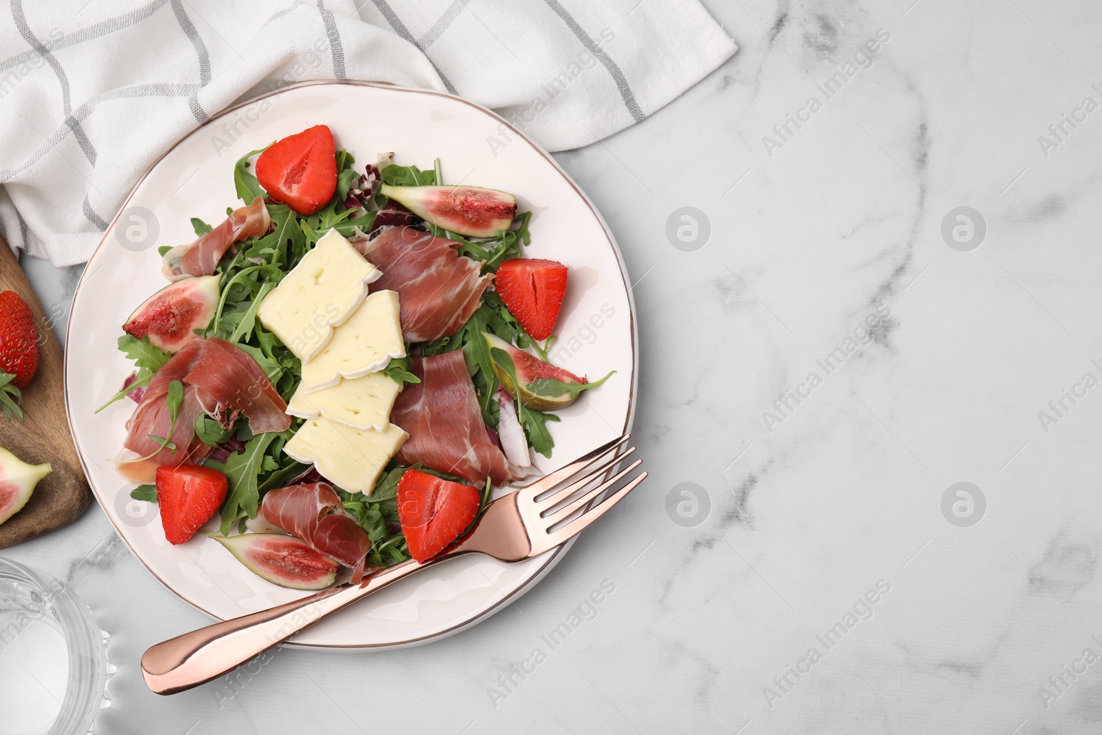 Photo of Tasty salad with brie cheese, prosciutto, strawberries and figs served on white marble table, top view. Space for text