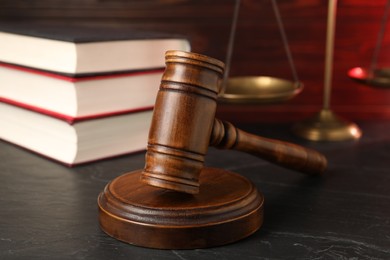 Photo of Wooden gavel, scales and stack of books on dark textured table, closeup