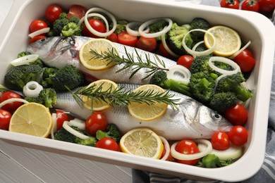 Raw fish with vegetables and lemon in baking dish on white wooden table