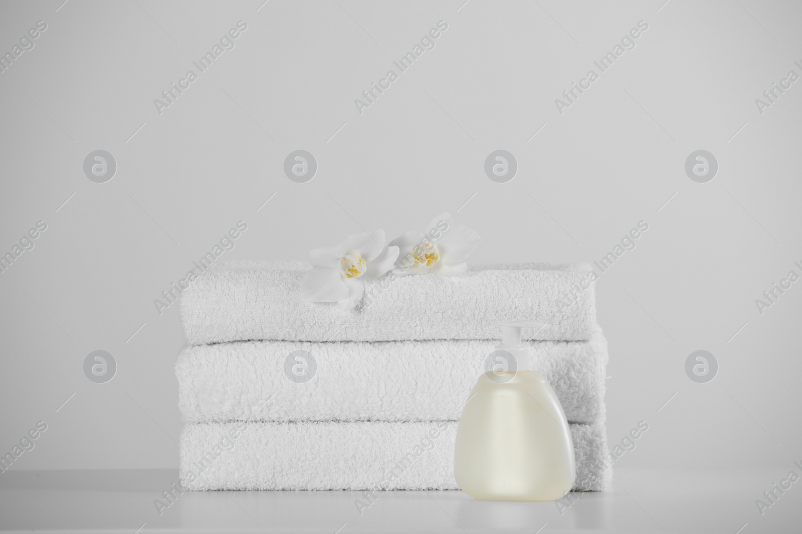 Photo of Soft folded towels, orchid flowers and dispenser on white table