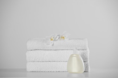 Soft folded towels, orchid flowers and dispenser on white table
