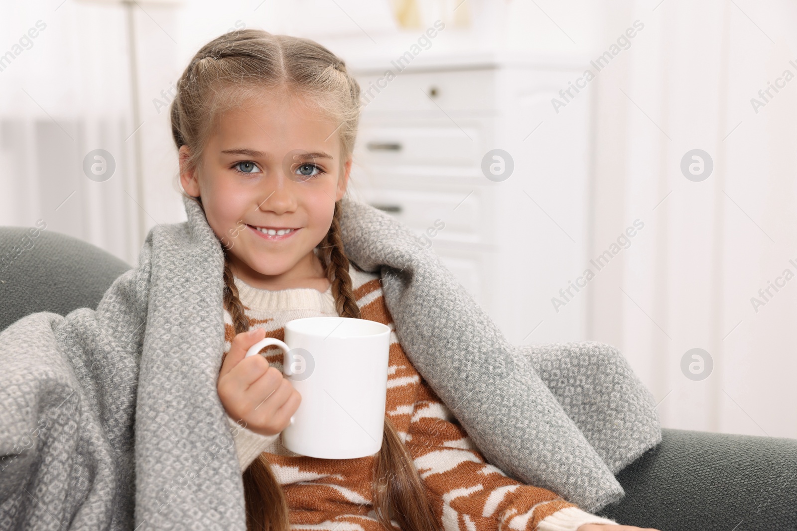 Photo of Happy girl under plaid with white ceramic mug on sofa at home, space for text