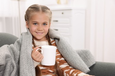 Photo of Happy girl under plaid with white ceramic mug on sofa at home, space for text