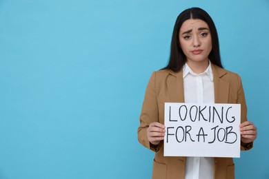 Young unemployed woman holding sign with phrase Looking For A Job on light blue background, space for text