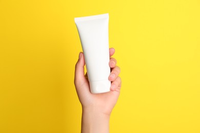 Photo of Woman holding tube of face cream on yellow background, closeup